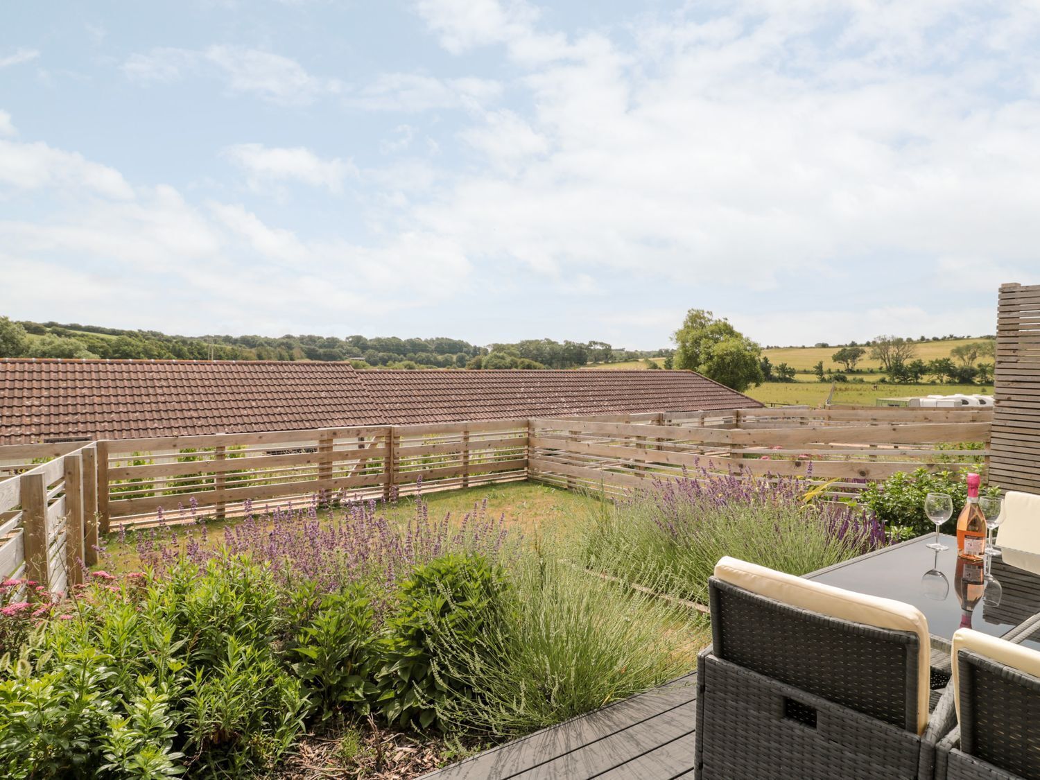 A patio area with a table and chairs, surrounded by a wooden fence and lush greenery.