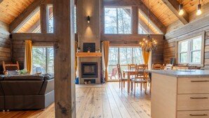 A spacious cabin with a large living area, a fireplace, wooden floors, and large windows offering views of the outdoors.