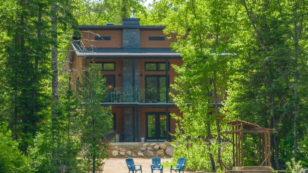 Un chalet au bord du lac, avec des fondations en pierre, de grandes fenêtres et un balcon.