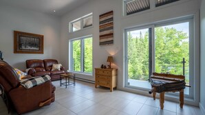 Un salon spacieux avec un canapé en cuir, un meuble en bois et une grande fenêtre donnant sur la forêt.