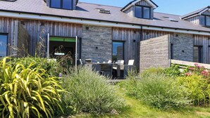 A modern house with a sloped roof, large windows, and a garden area with various plants. - Overcombe Mill (Weymouth)