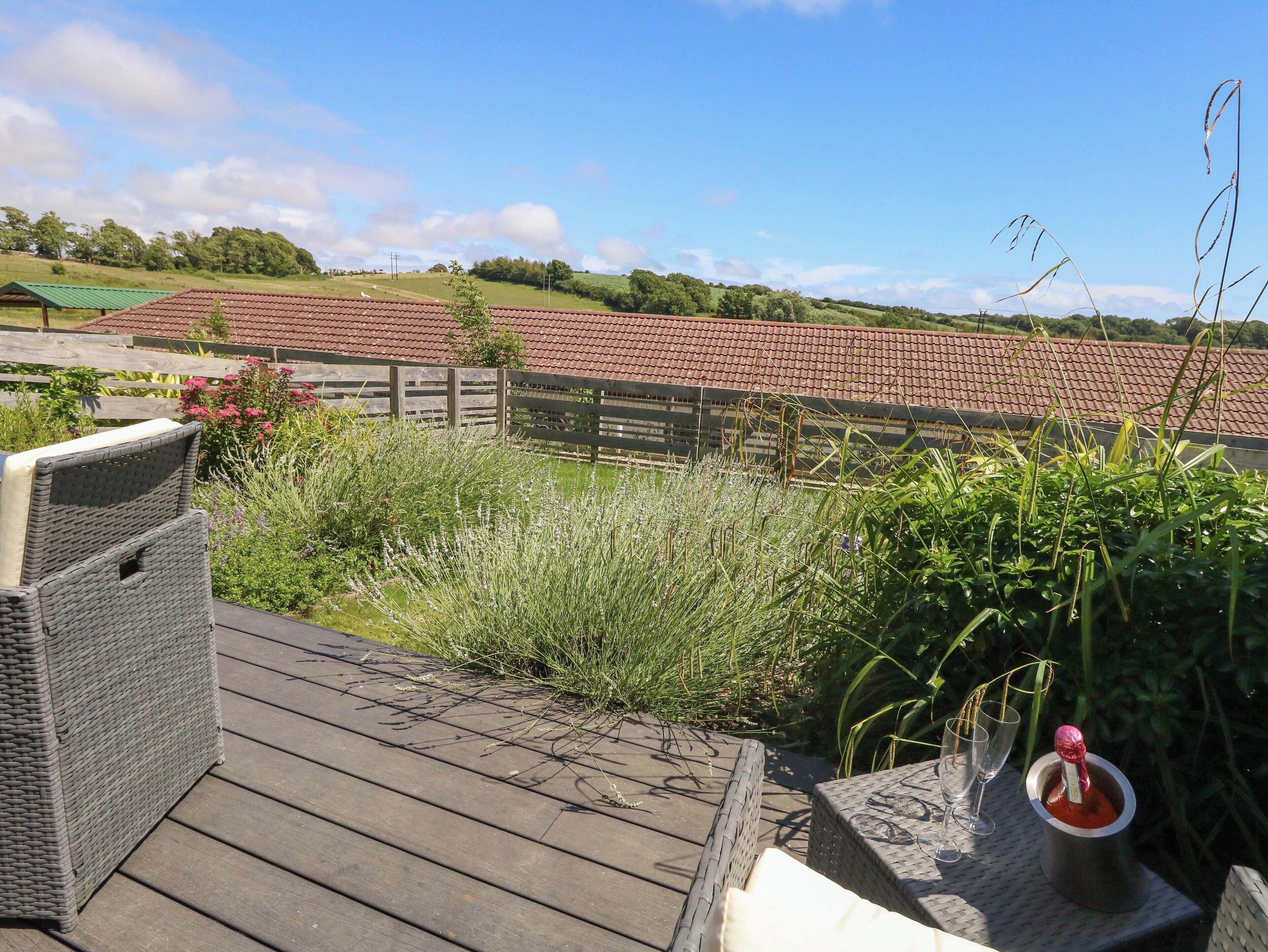 Une terrasse en bois, meublée de meubles en osier, avec une table sur laquelle se trouve une boisson.