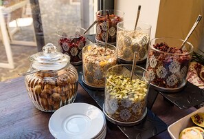A variety of food items in glass containers on a table, including granola, nuts, and dried fruits. - ART HOTEL (Sibiu)