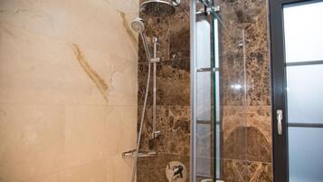 A bathroom with a glass shower enclosure, marble tiles, and a toilet paper dispenser.