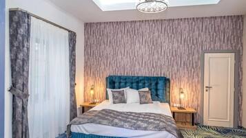 Quarto com cama grande, duas luminárias de cabeceira, iluminação de teto e piso estampado.