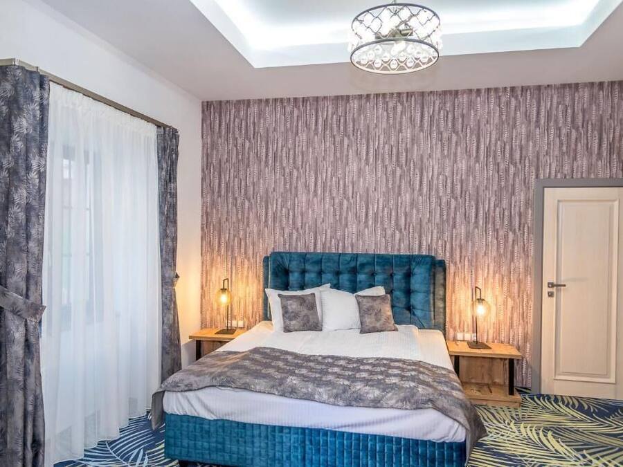 Quarto com cama grande, duas luminárias de cabeceira, iluminação de teto e piso estampado.
