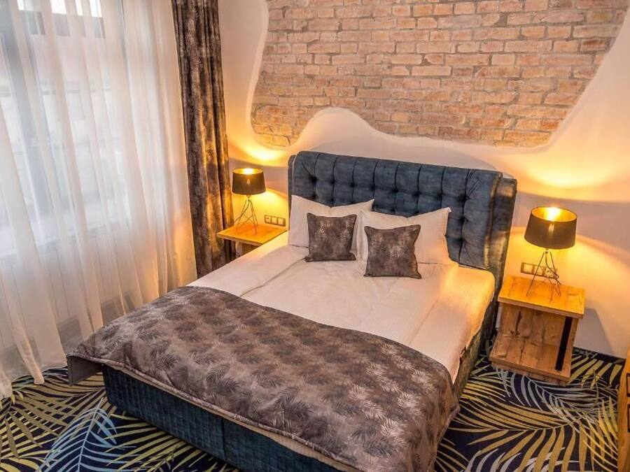 A bedroom with a brick wall, a tufted headboard, two bedside lamps, a patterned bedspread, and a zebra-striped floor.