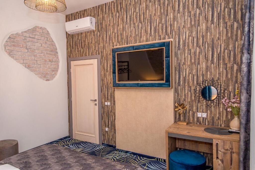 A small, cozy room with a bed, a wooden dresser, a mirror, and a wall with a textured pattern.