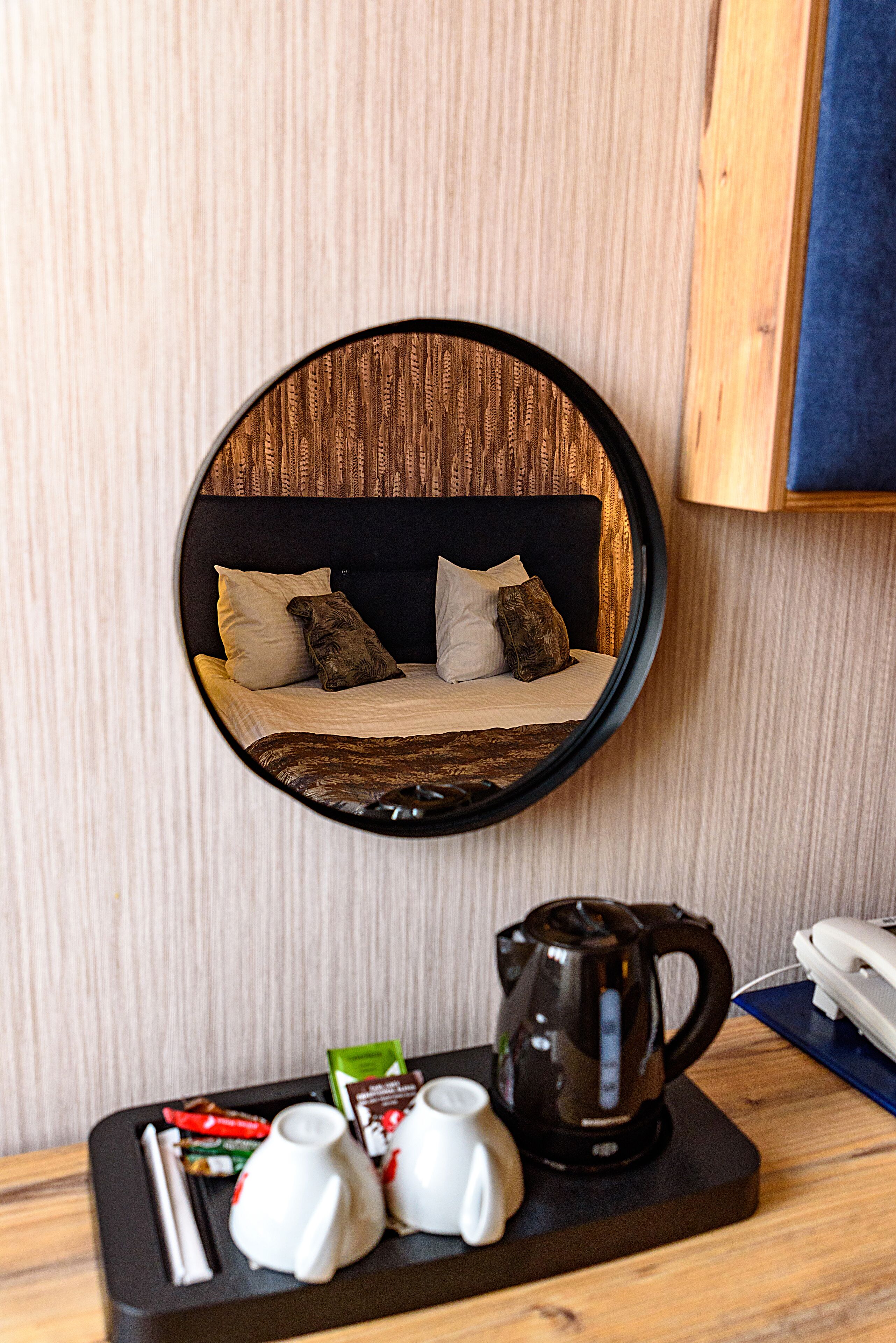 A round mirror reflecting a bed with pillows, a tray with a kettle, cups, and snacks.