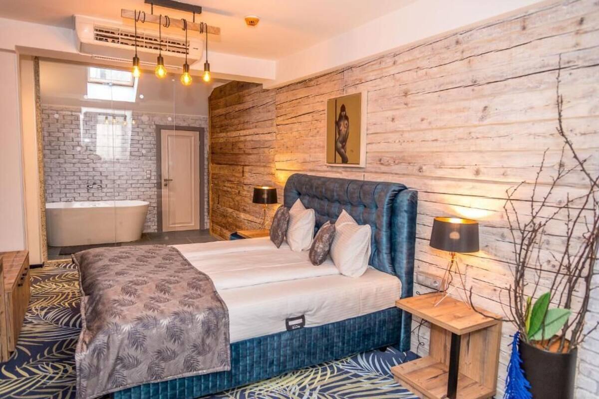 A modern bedroom with a large bed, a wooden headboard, a nightstand, and a wall-mounted lamp.