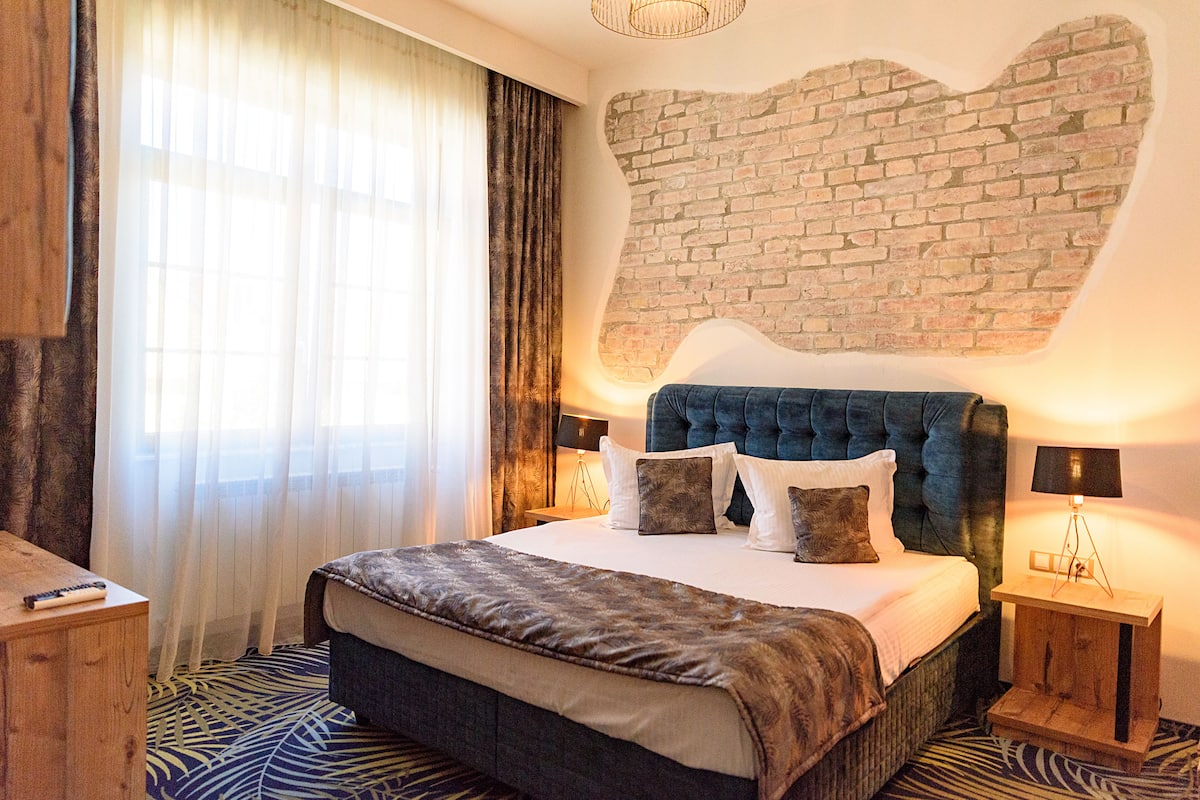 A hotel room with a large bed, a brick wall accent, a wooden nightstand, and a lamp.