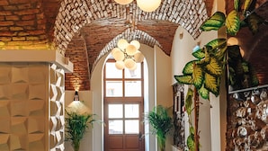 A hallway with a brick ceiling, large potted plants, and a wooden door at the end. - ART HOTEL (Sibiu)