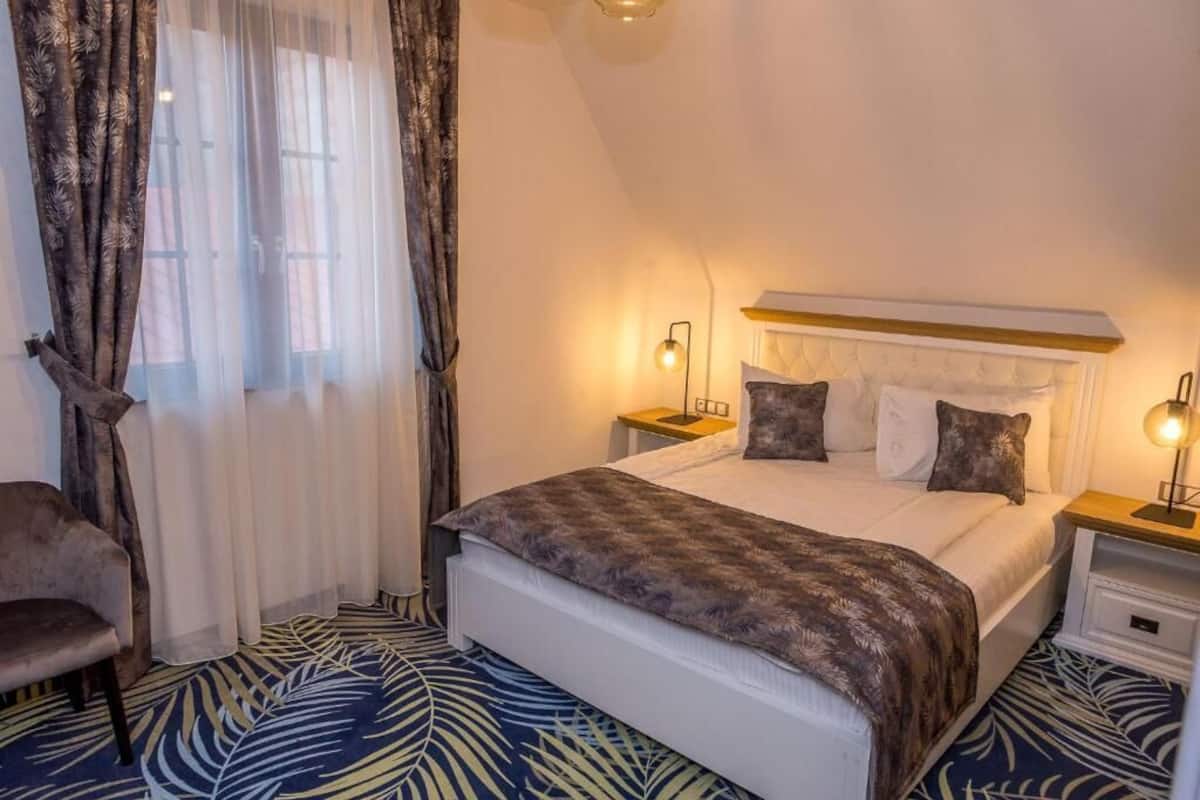 A hotel room with a bed, two bedside tables, a chair, and a window with curtains.