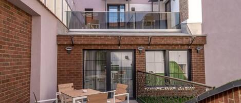 A modern building with a glass balcony, a brick facade, and a wooden table with chairs.