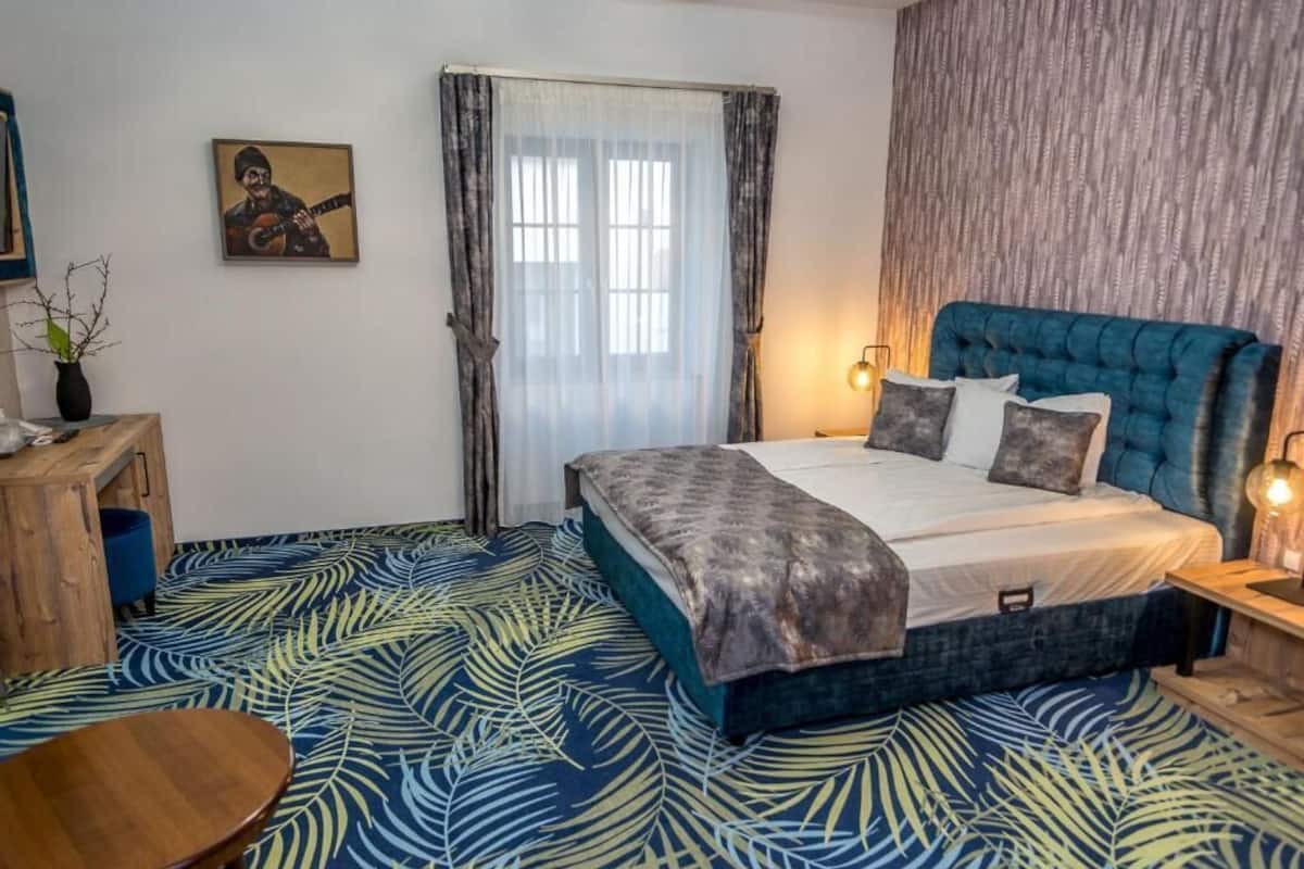 A bedroom with a large bed, a wooden nightstand, a desk, and a chair.