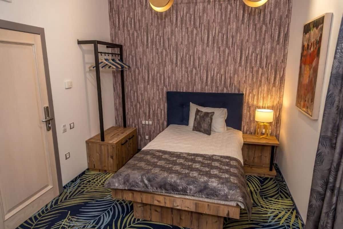 A bedroom with a bed, wooden nightstands, a wardrobe, and a patterned floor.