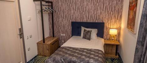 Un dormitorio con una cama, mesitas de noche de madera, un armario y suelo estampado.