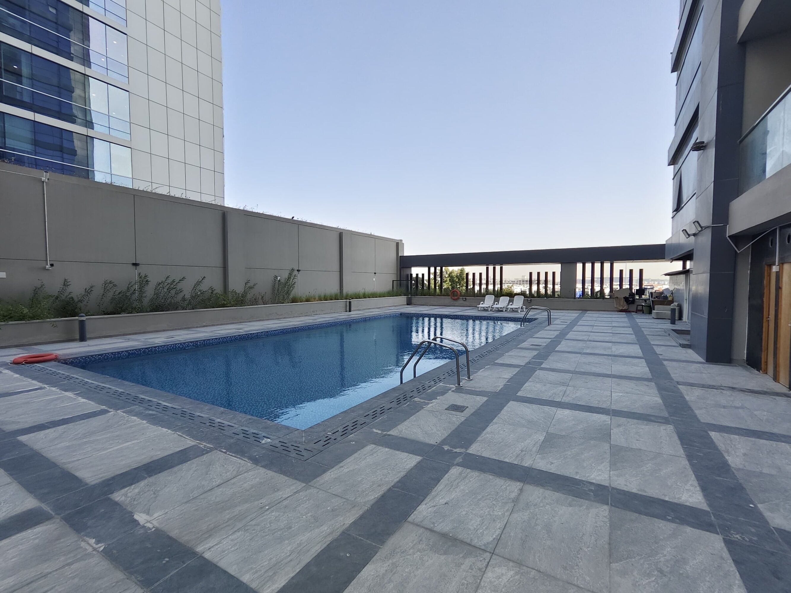 Un espace piscine aménagé sur le toit, avec une piscine à l’eau d’un bleu limpide, un sol carrelé et quelques chaises longues.