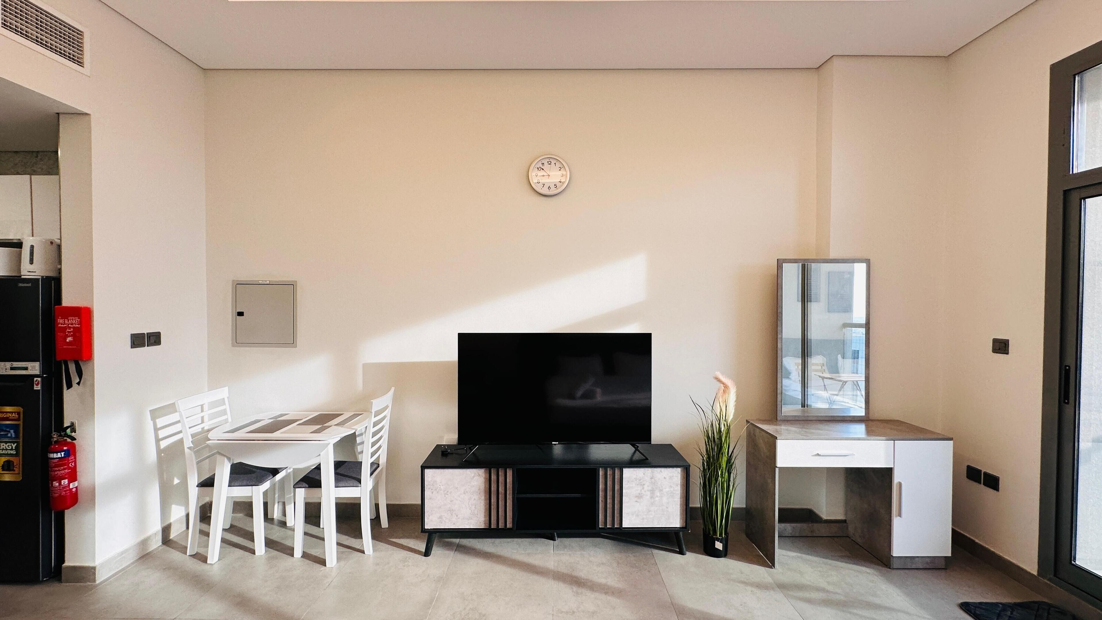 Una sala moderna con televisor de pantalla plana, una mesa de comedor con sillas, un escritorio pequeño y una planta en maceta.