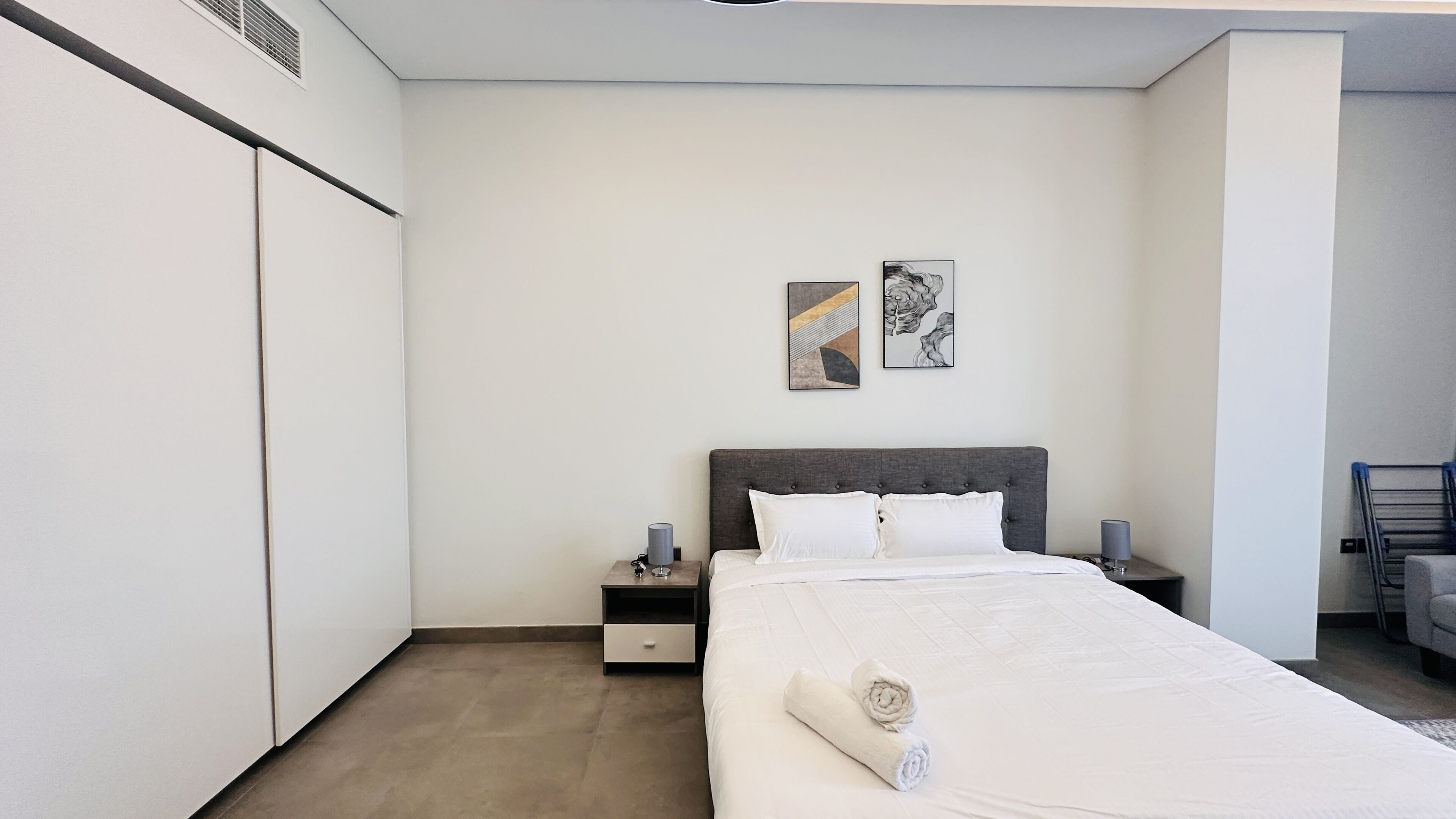 A modern bedroom with a large bed, two bedside tables, a wardrobe, and abstract wall art.