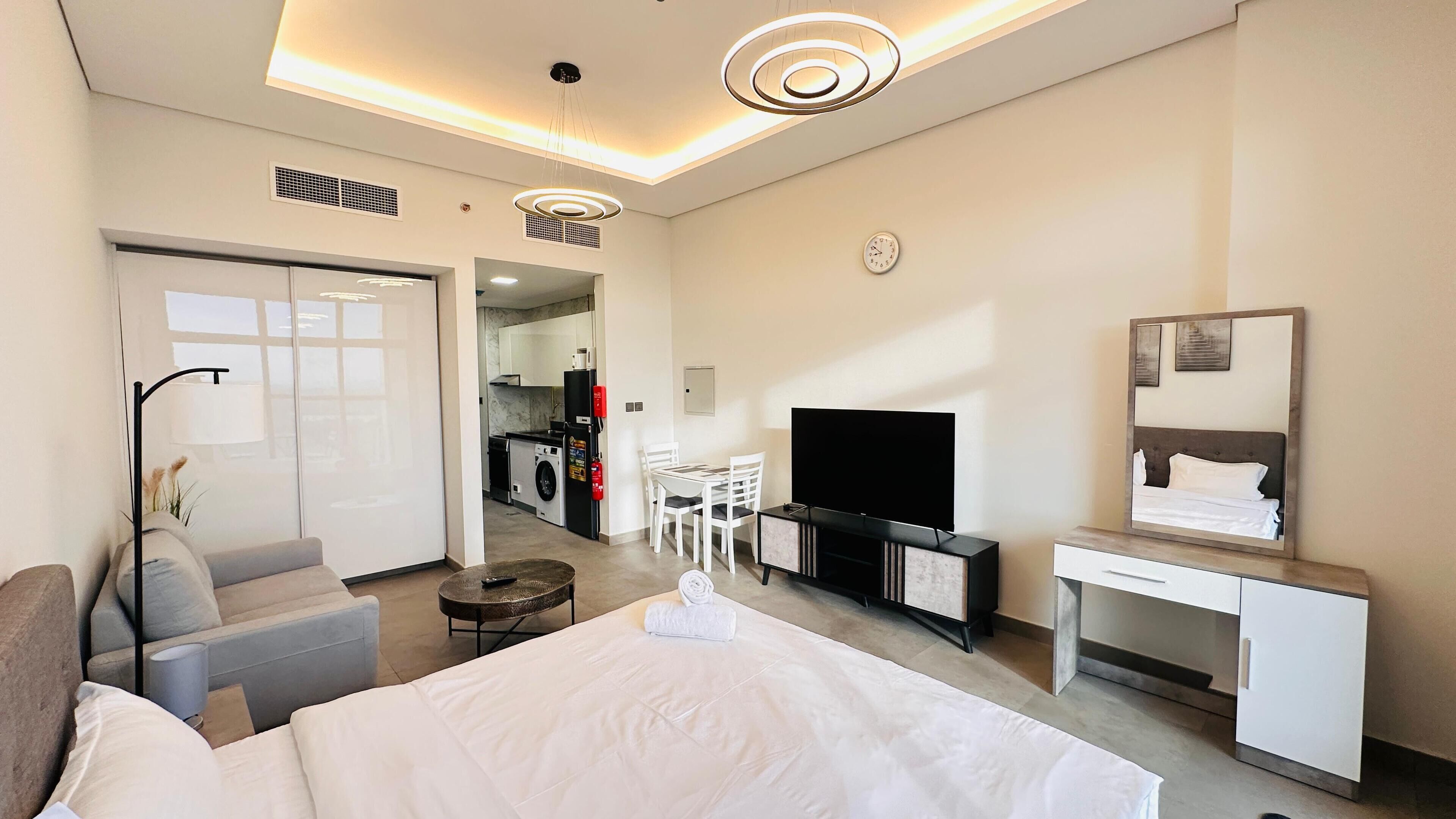Une chambre d’hôtel moderne avec un lit, un bureau, une télévision et, au fond, une kitchenette.