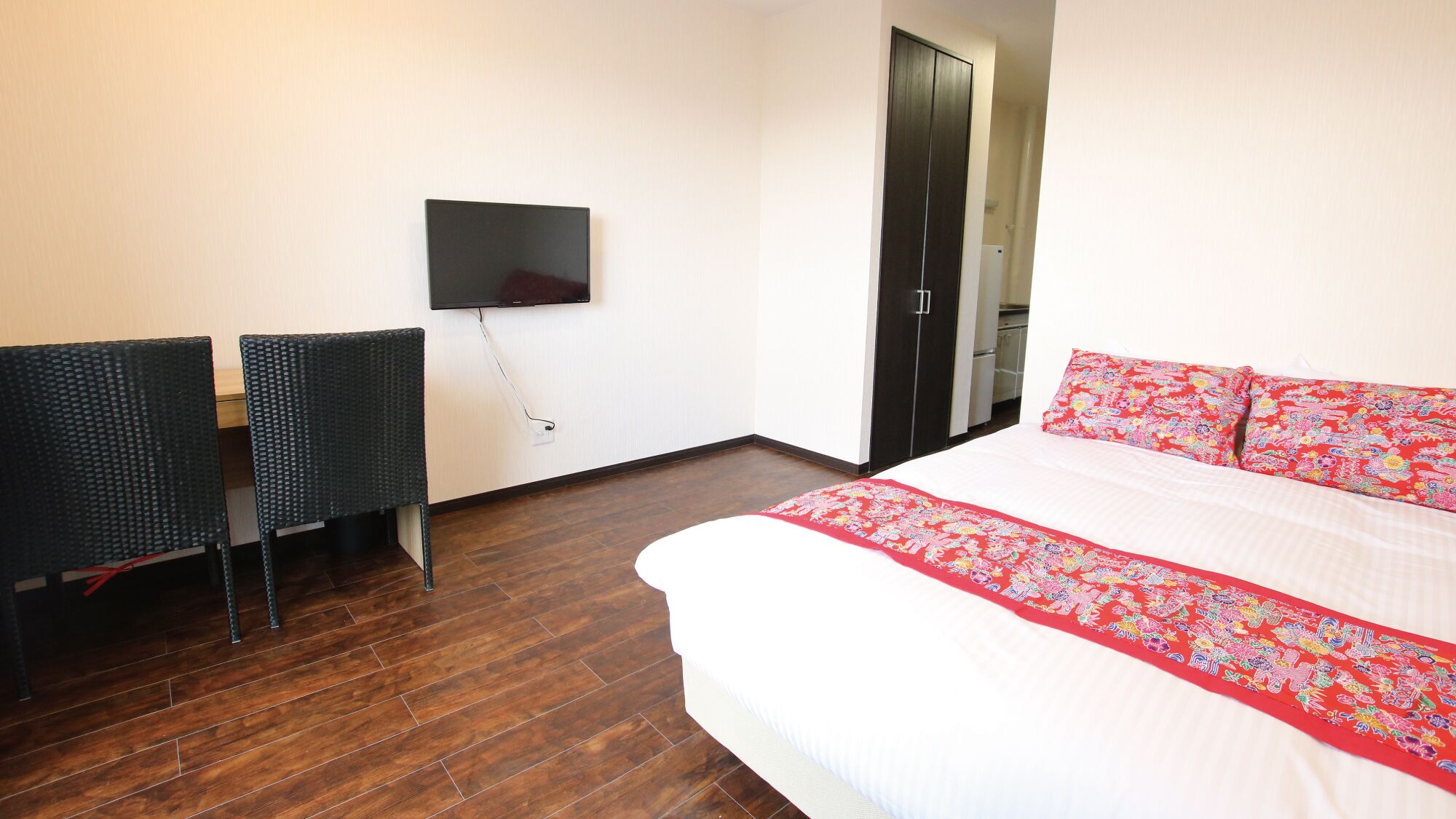 Ein Hotelzimmer mit einem Bett, einem an der Wand montierten Fernseher, zwei Sesseln und einem Kleiderschrank.