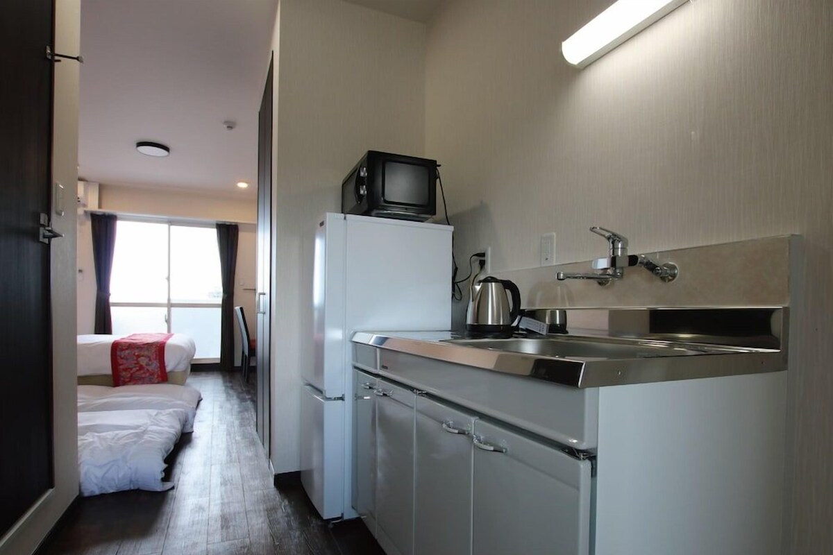A compact kitchen with a refrigerator, stove, and a microwave on top.