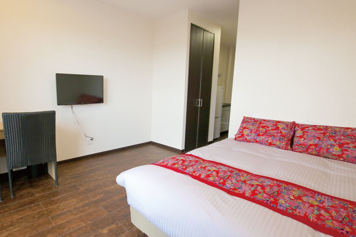 Une chambre d’hôtel comprenant un lit, un téléviseur fixé au mur, un bureau avec deux chaises et une armoire.