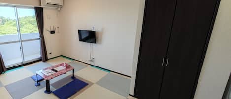 A room with a large sliding door leading to a balcony, a flat-screen TV mounted on the wall, and a wardrobe with two doors.