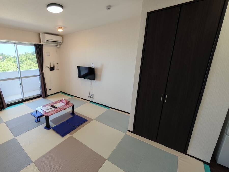 A room with a large sliding door leading to a balcony, a flat-screen TV mounted on the wall, and a wardrobe with two doors.
