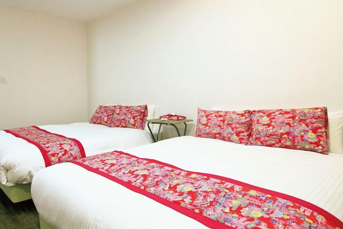 A hotel room with two beds, each with a red floral bedspread and matching pillows.