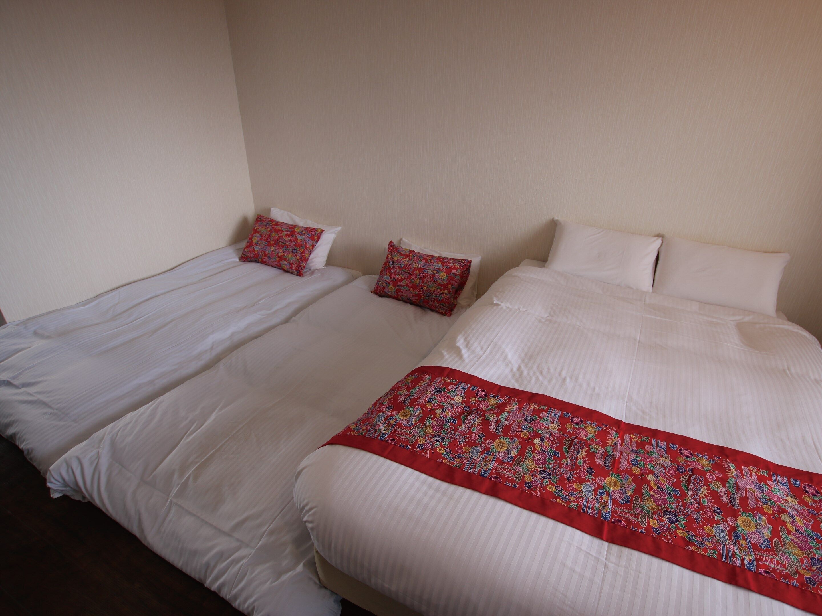 A hotel room with two single beds, each with white bedding and red decorative pillows.