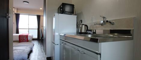 A compact kitchen with a refrigerator, a microwave, a kettle, and a sink.