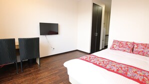Habitación de hotel con cama, televisor montado en la pared, escritorio con dos sillas y armario.
