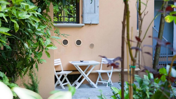 A small outdoor seating area with a table and chairs, surrounded by plants and a building wall. - il Nespolo (Bologna)