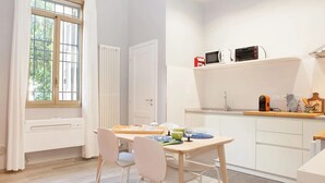 A modern kitchen with a dining area, white cabinetry, a built-in microwave, and a window with curtains. - il Nespolo (Bologna)