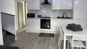 Une cuisine moderne avec des armoires blanches, une cuisinière noire, un four à micro-ondes et un évier. On y trouve une table à manger avec des chaises et un tapis sur le sol.