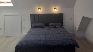 Une chambre avec un grand lit, deux lampes fixées au mur, un puits de lumière et une armoire blanche.