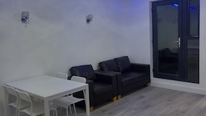 Un salon moderne avec une table et des chaises blanches, un canapé en cuir noir et une porte-fenêtre coulissante.