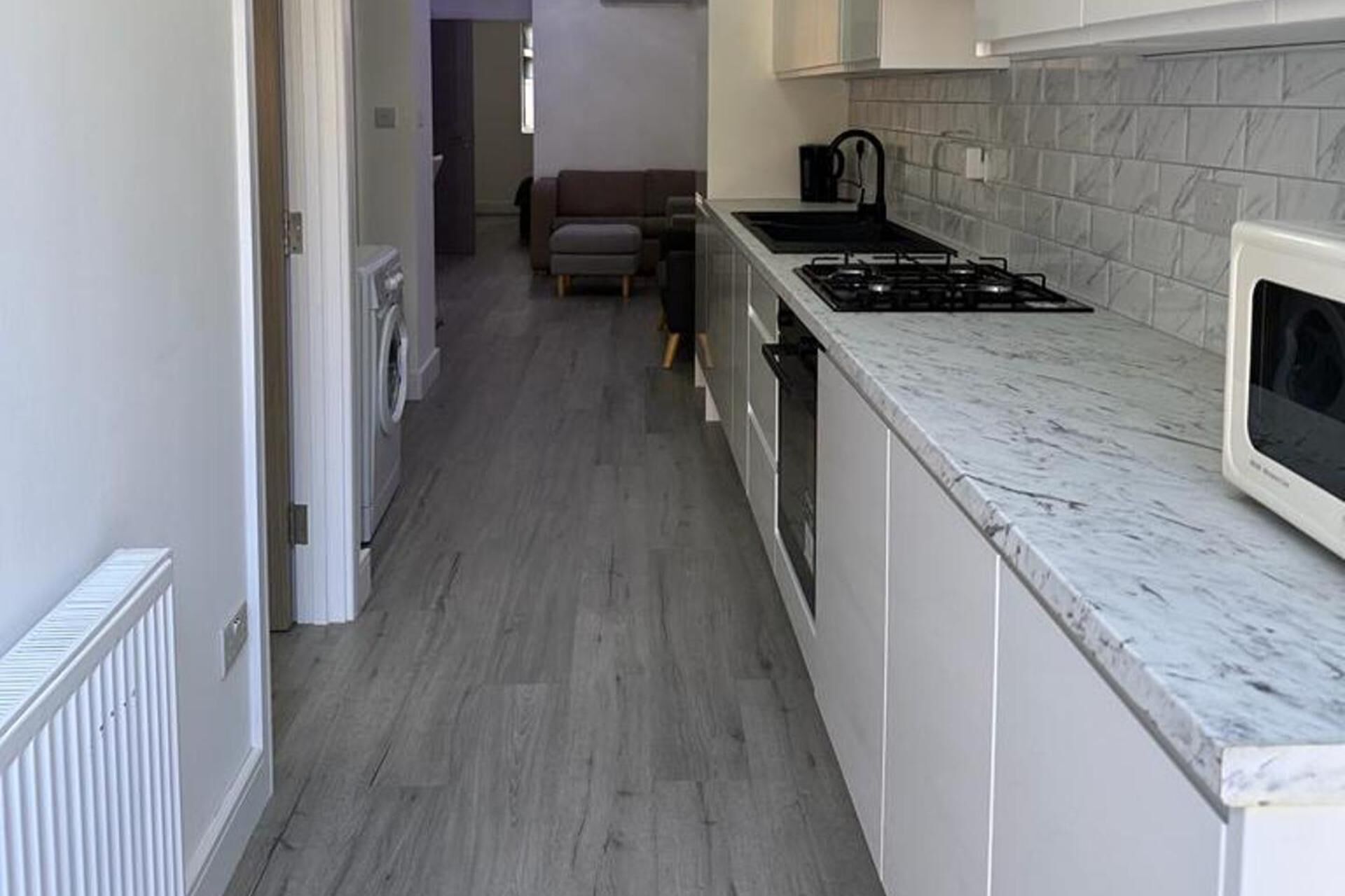 A narrow kitchen with a gas stove, a microwave, and a washing machine in the background.