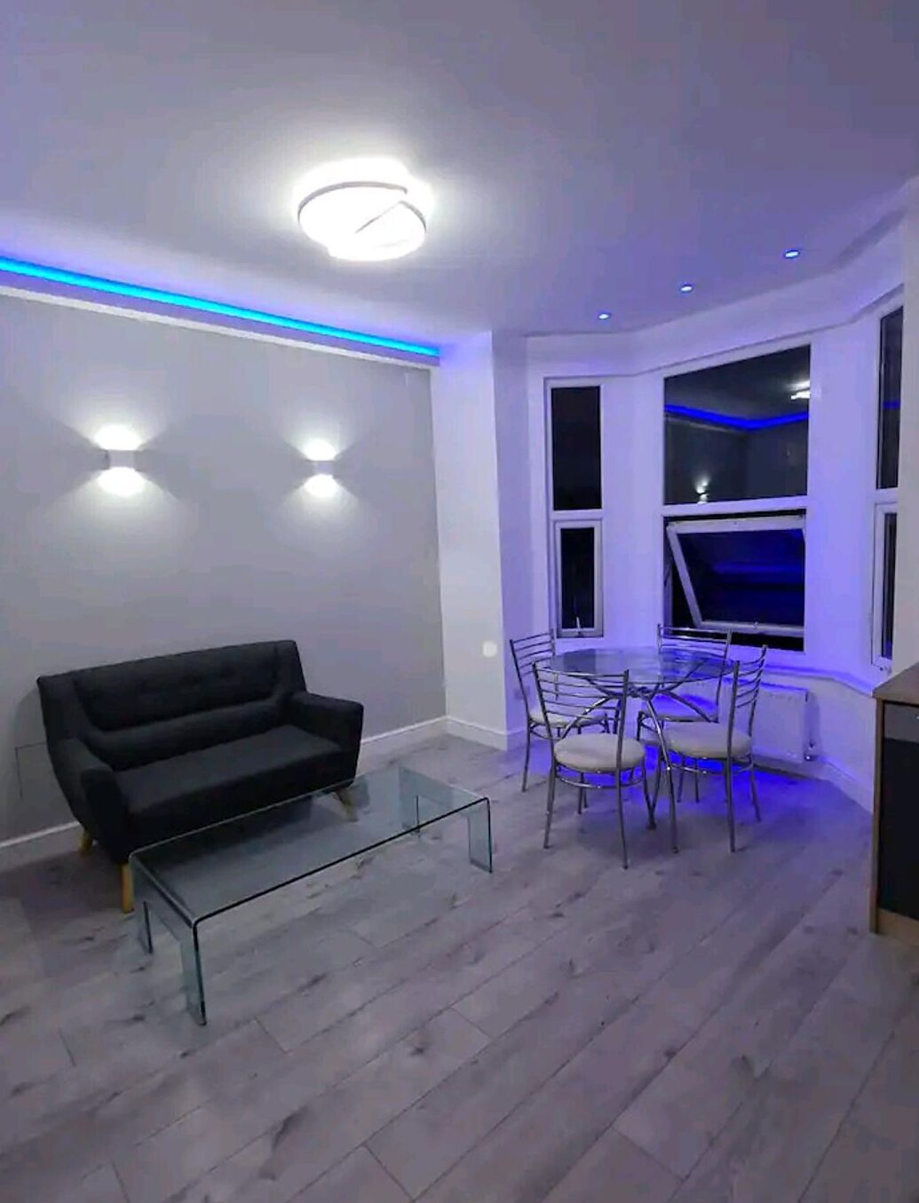 A modern living room with a black sofa, a glass coffee table, and a dining area with a table and chairs.