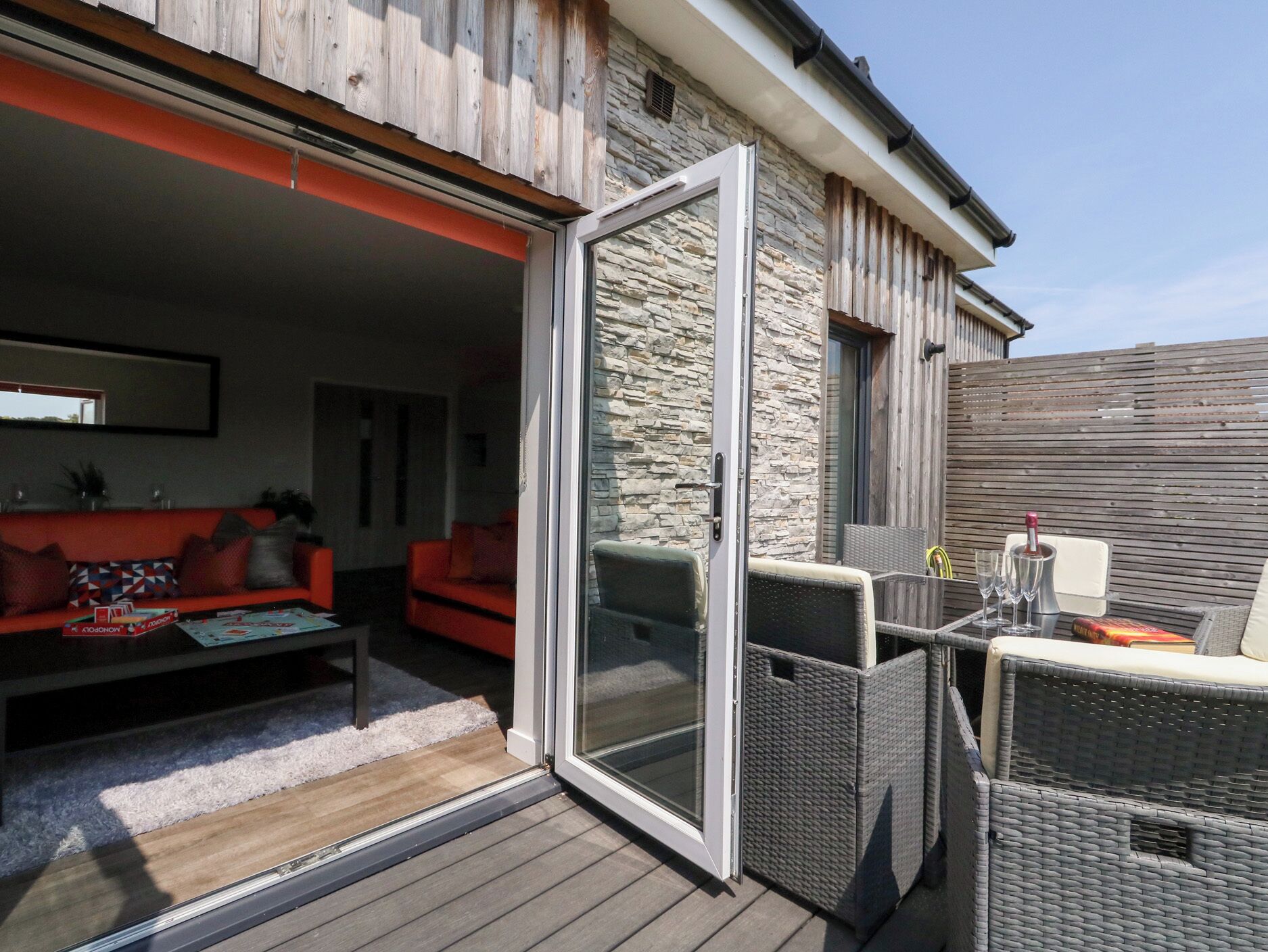 Eine offene Terrasse mit Steinwand, Korbmöbeln und einem roten Sofa.