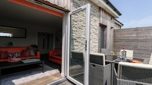 Eine offene Terrasse mit Steinwand, Korbmöbeln und einem roten Sofa.