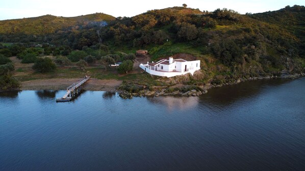 Une maison blanche dotée d’un balcon, située sur une colline et offrant une vue sur un lac paisible.