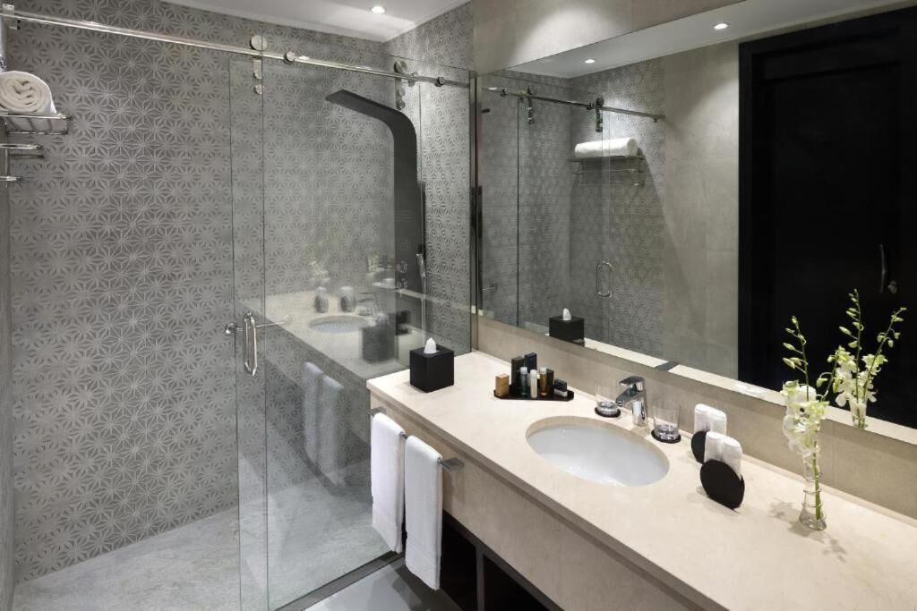 A modern bathroom with a glass-enclosed shower, a large mirror, and a beige vanity with toiletries.