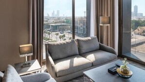 Habitación de hotel moderna con un ventanal grande que ofrece vistas a la ciudad, un sofá, una mesita y una lámpara.