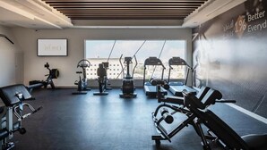 Un gimnasio moderno con equipos de ejercicio variados, un ventanal grande y un cartel motivacional en la pared.