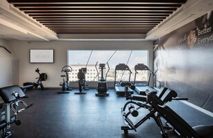 Un gimnasio moderno con equipos de ejercicio variados, un ventanal grande y un cartel motivacional en la pared.