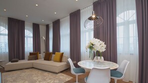 A modern living room with a sectional sofa, a round dining table with chairs, and a large window with curtains. - Roof Suite - Castello il Codirosso Accomodation Hotel (Cesate)