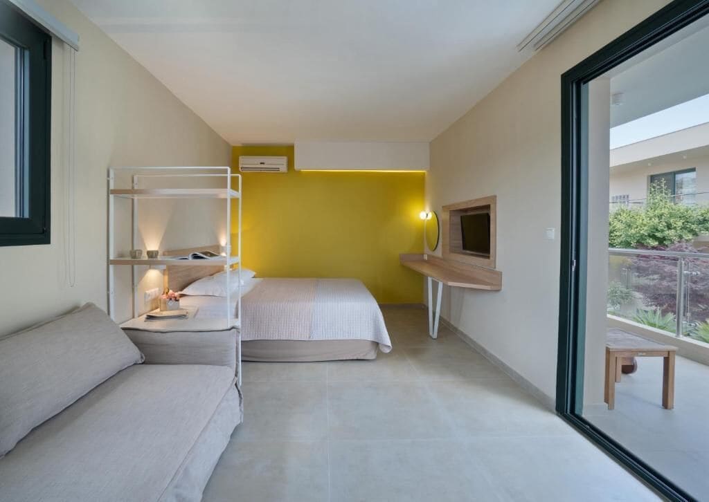 Camera d'albergo compatta con un letto a castello, una divisa, un tavolino, una TV e un balcone con vista.